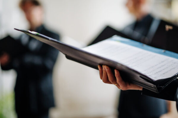 Hands holding music folders represent the Voices of Hope Community Chorus members singing.